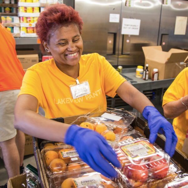 a woman at a food pantry holds a carton of tomatoes